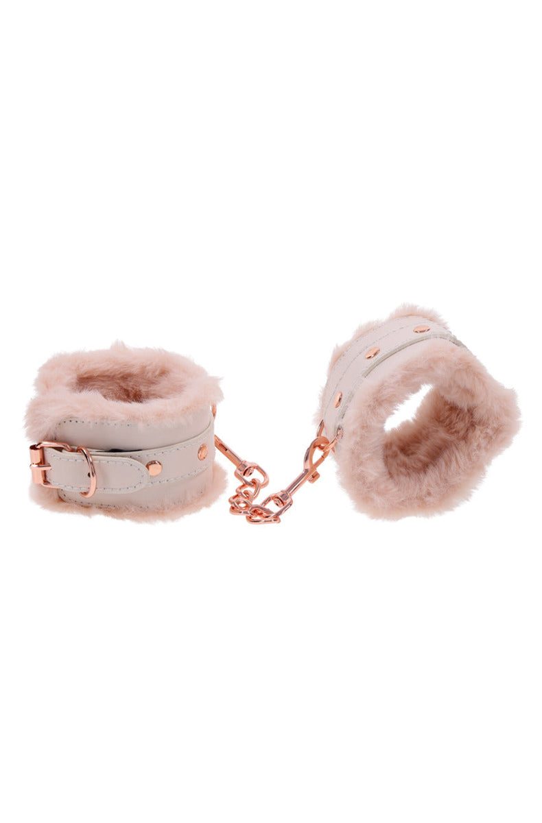 Pair of pale cream faux leather wrist cuffs with peach fur lining and a short rose-gold connecting chain.