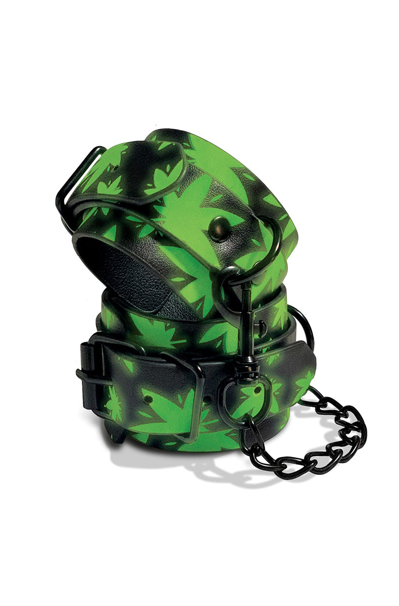 Pair of black faux leather wrist cuffs with bright green cannabis-leaf print, black buckles, and a black connecting chain.