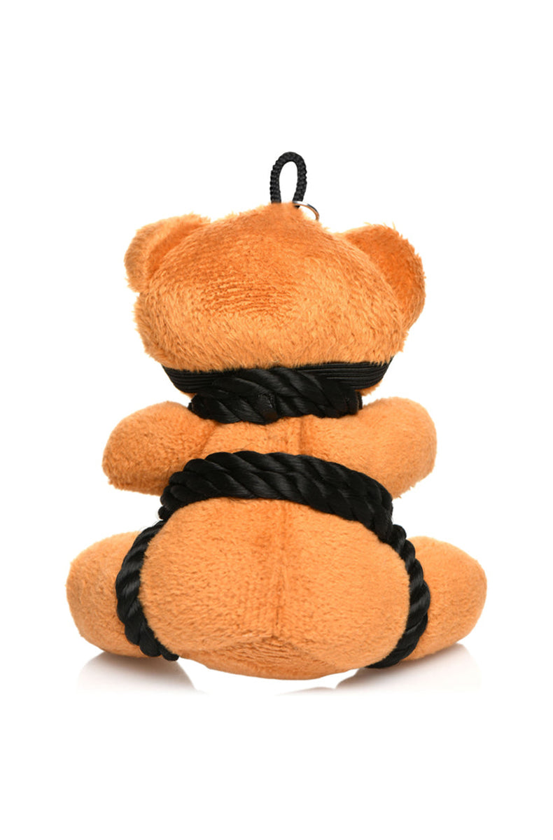 Side view of tan plush teddy bear keychain showing black shibari rope wraps and black blindfold strap.