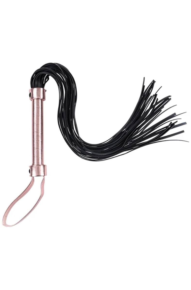 Side view of the brat flogger laid flat, thin black falls fanning out from a rose-gold wrapped handle and loop.