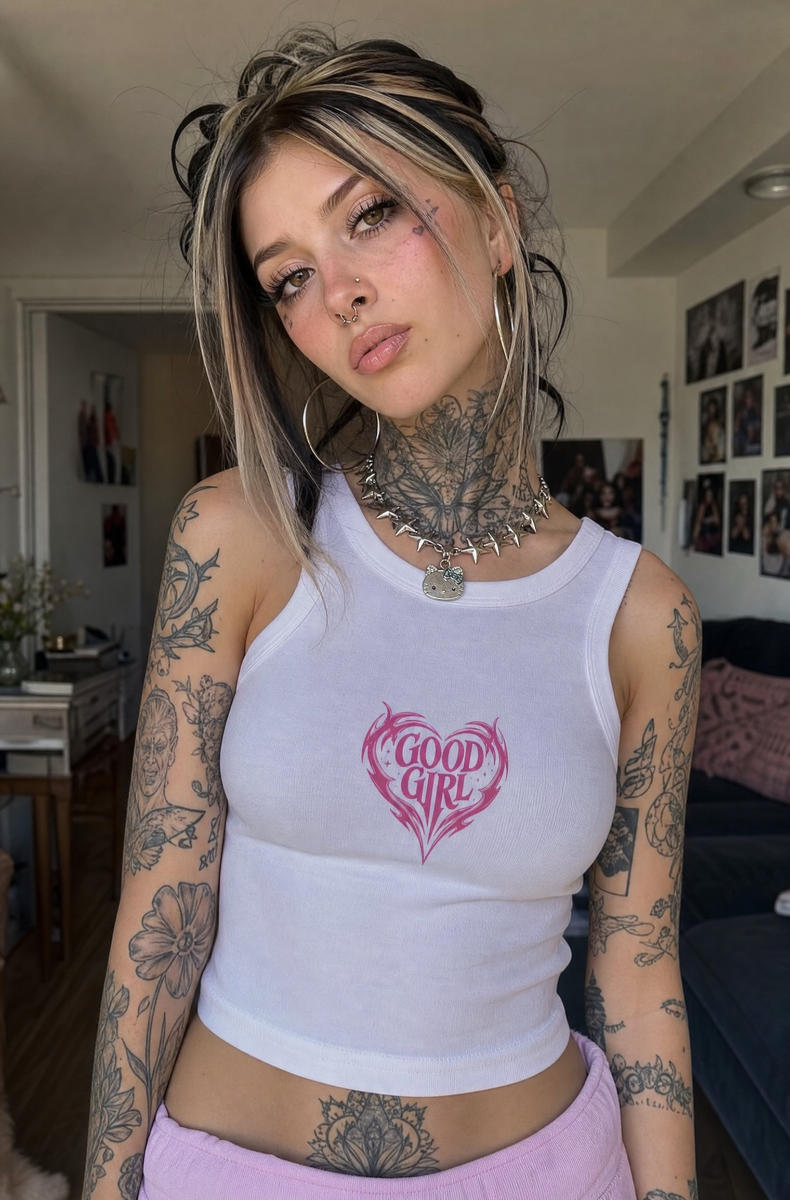 White Good Girl racerback tank with a pink tribal heart graphic, worn by a blonde model in an apartment.