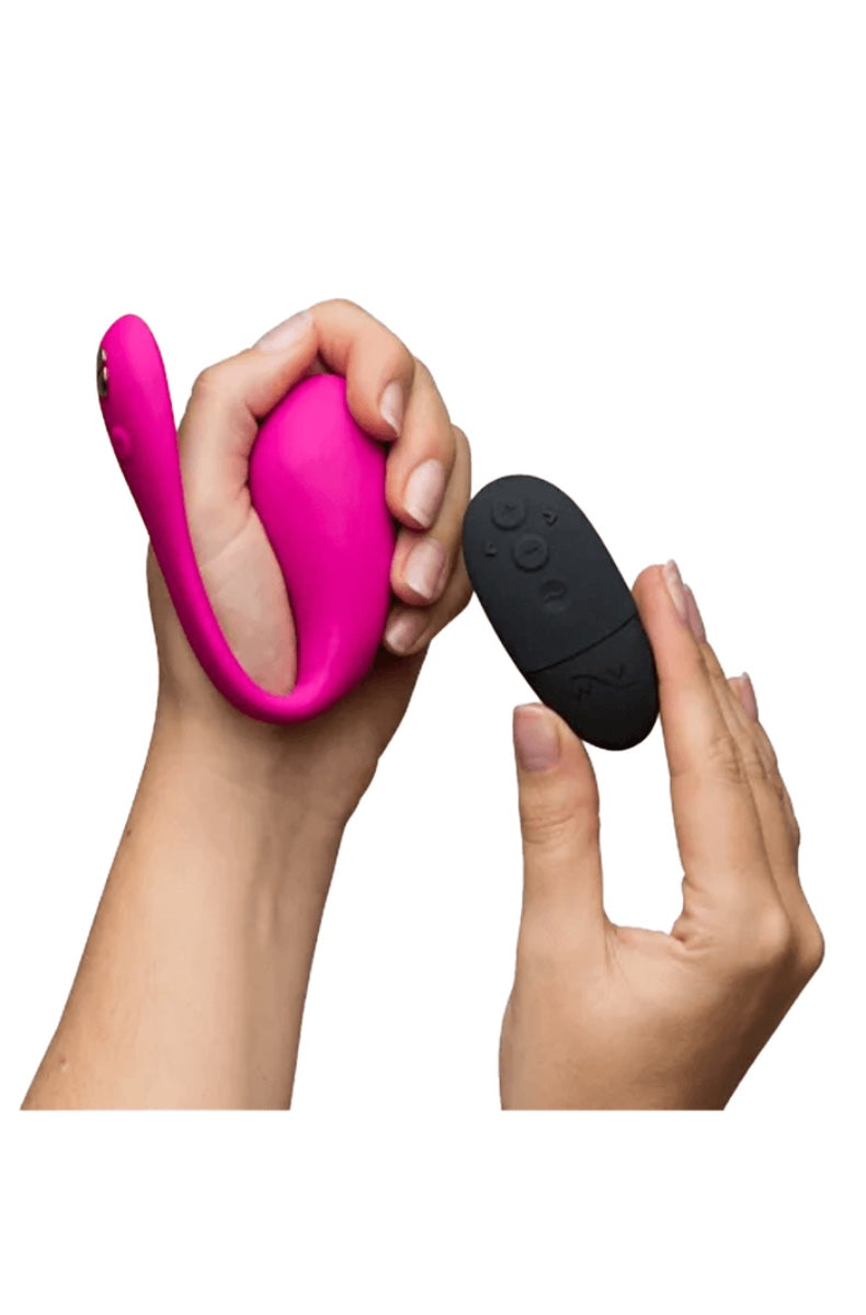 Hands holding pink wearable vibrator and black wireless remote with control buttons