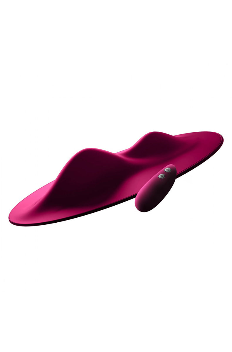Magenta silicone Vibepad grinding mat tilted up with raised central ridge and remote