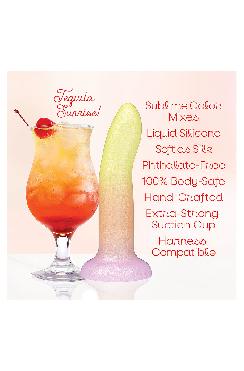Yellow, orange and pink ombre dildo beside a tequila sunrise cocktail: liquid silicone, suction cup, harness compatible