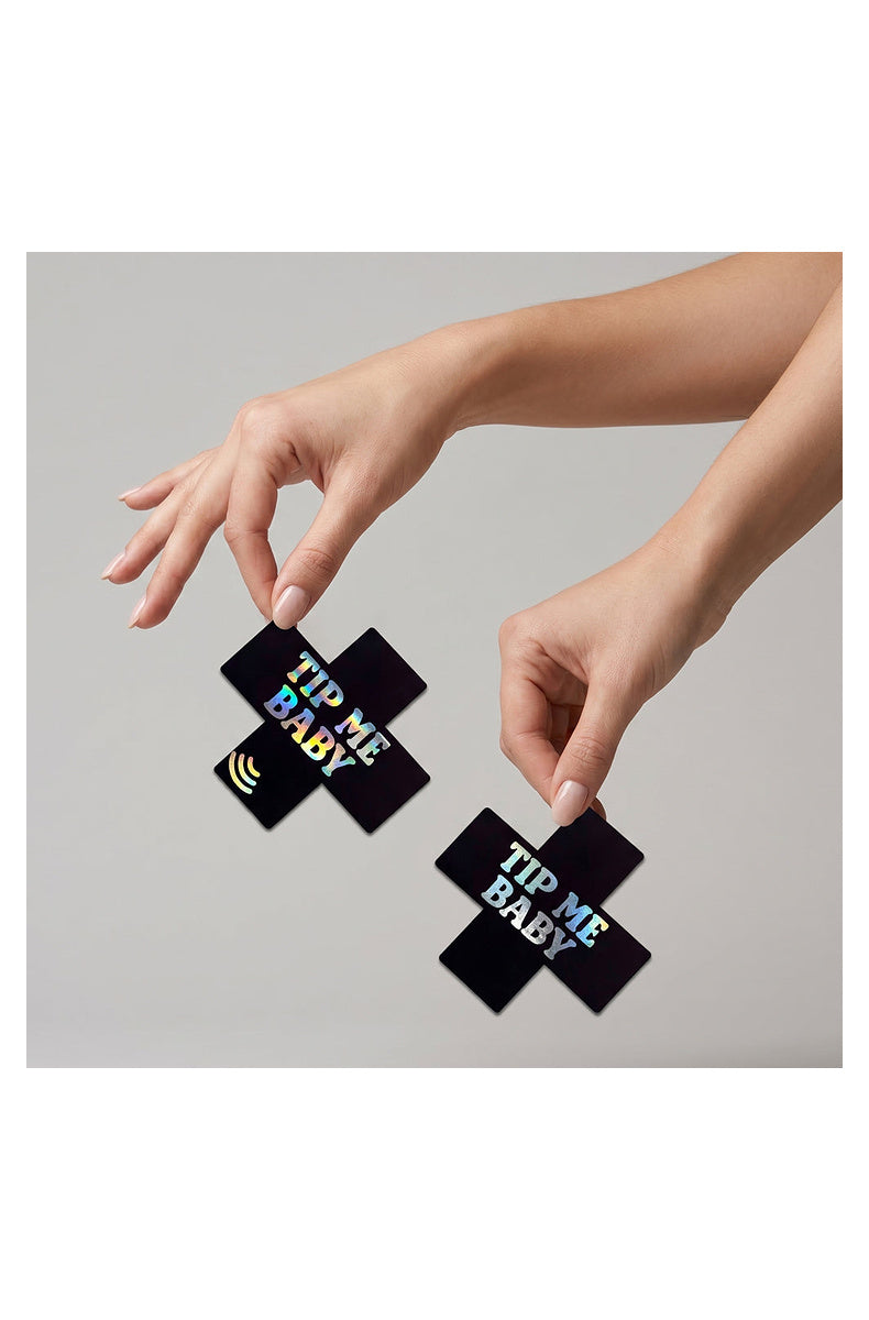 Two black TIP ME BABY cross pasties held between fingertips