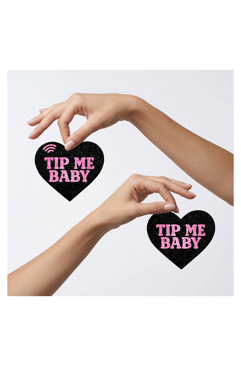 Two black glitter TIP ME BABY heart pasties held between fingertips