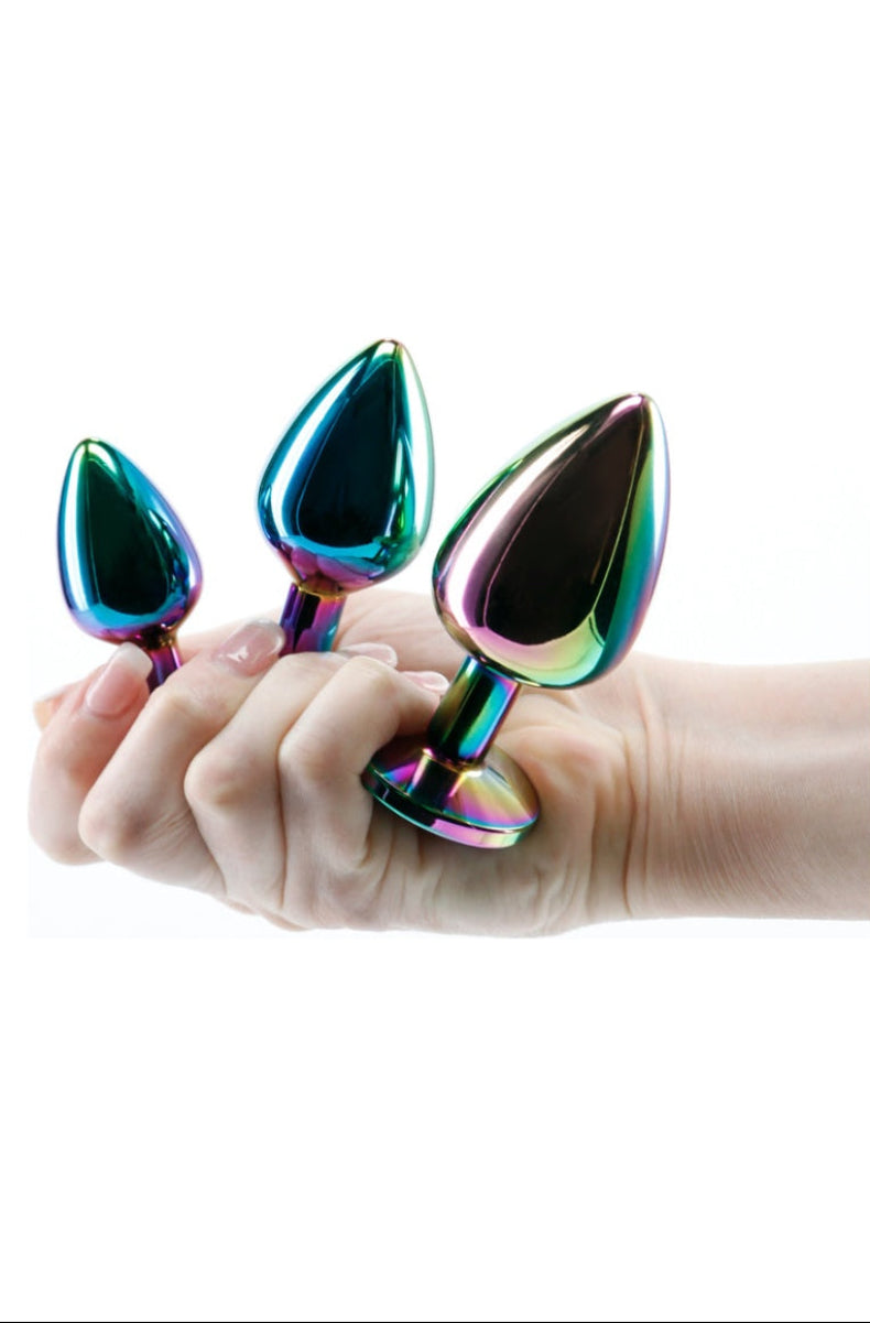 Three graduated rainbow metal butt plugs balanced on a hand for scale, smallest to largest