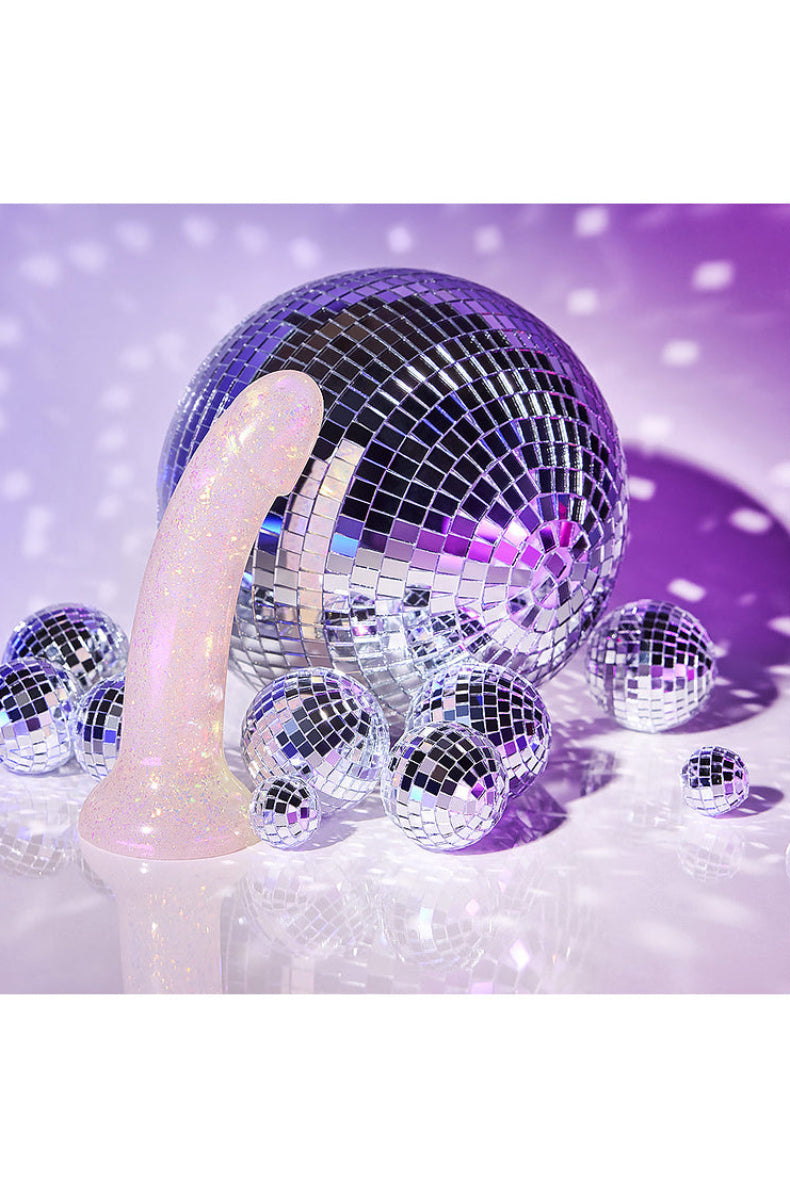 Clear gold glitter dildo lying among small disco balls in purple light