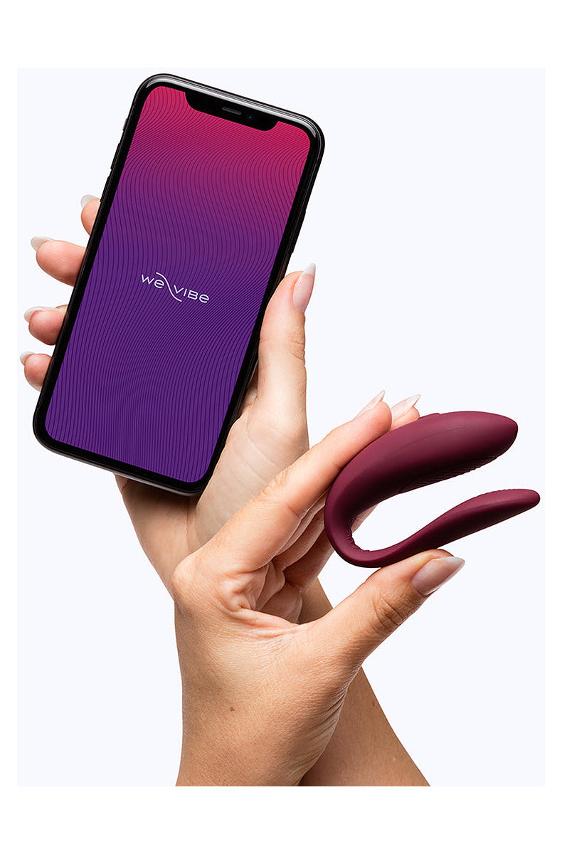 Hand holding the burgundy We-Vibe Sync Lite next to a phone with the We-Vibe app