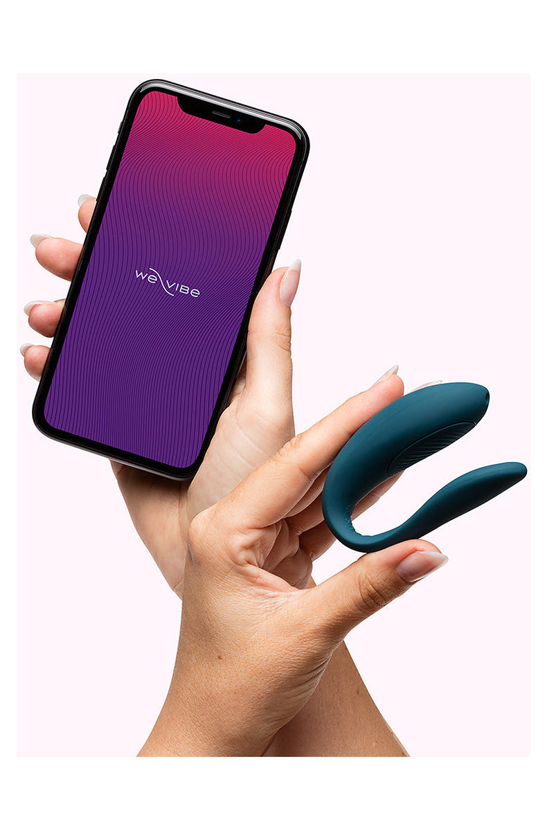 Hand holding the teal We-Vibe Sync Lite next to a phone with the We-Vibe app
