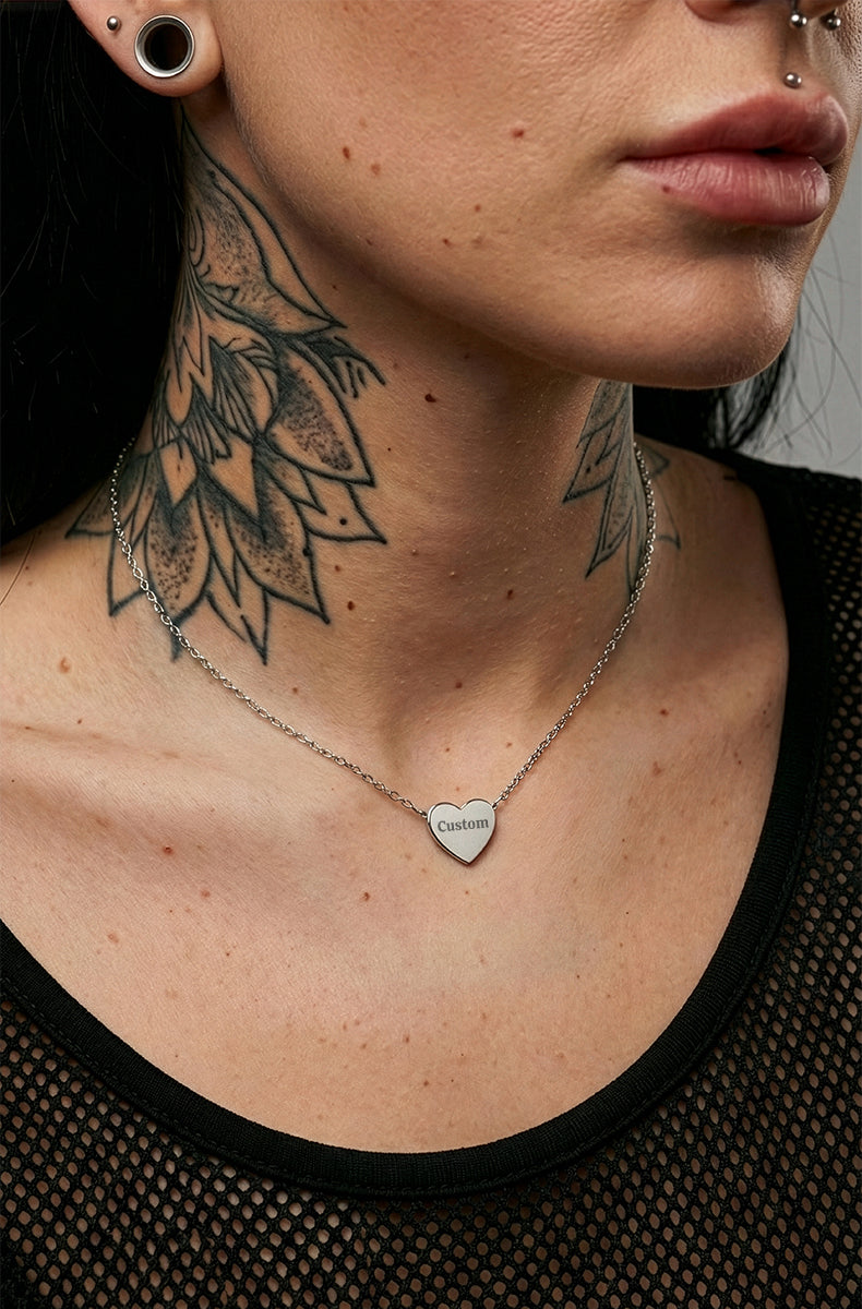Close-up of a person wearing a silver necklace with a heart pendant, showcasing neck tattoos.