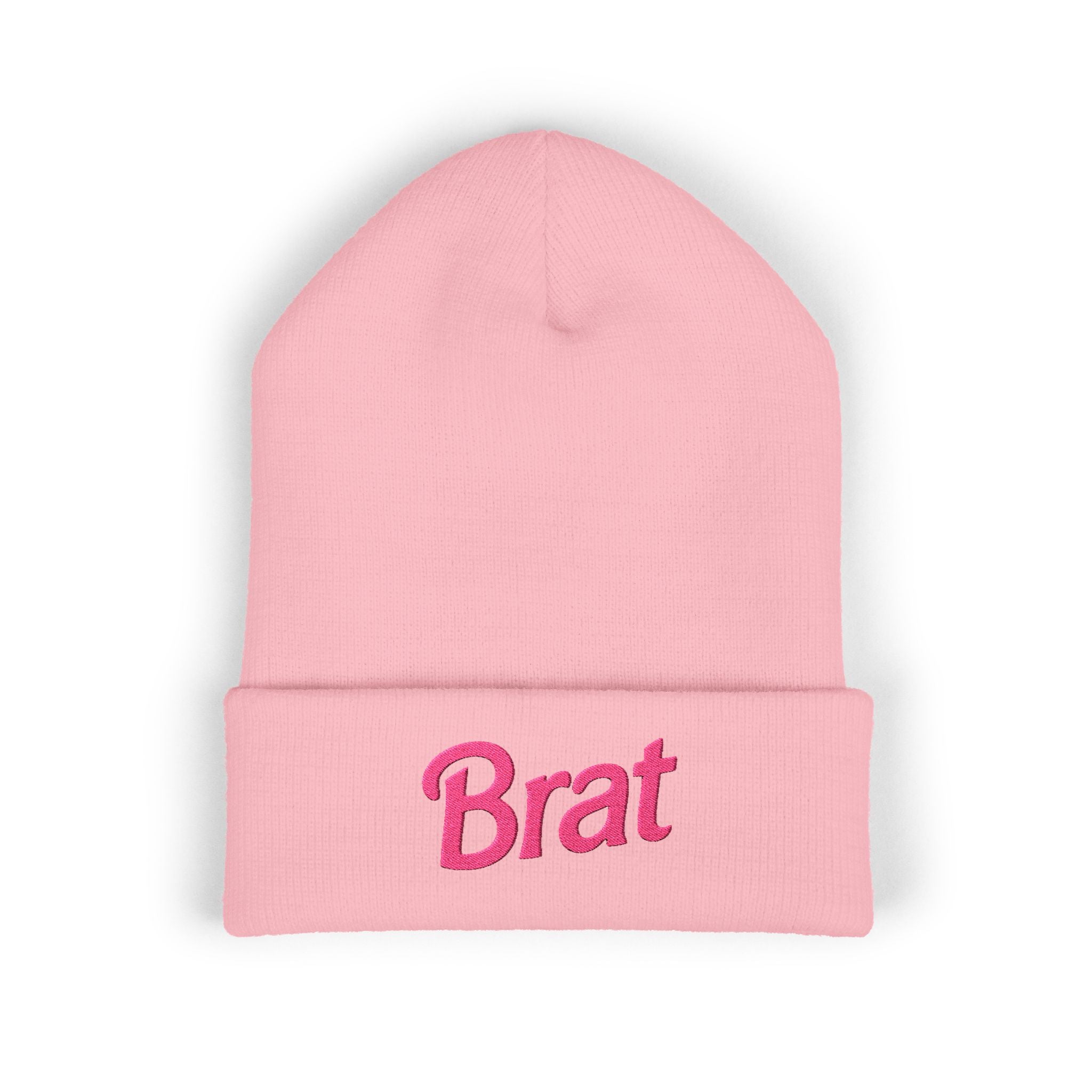 Soft pastel pink cuffed knit beanie with bold hot-pink "Brat" embroidery across the front of the cuff, worn by a model with pink hair.