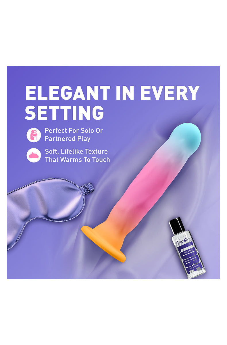 Aqua, pink and gold ombre dildo beside a satin sleep mask and lube, harness compatible for solo or partnered play