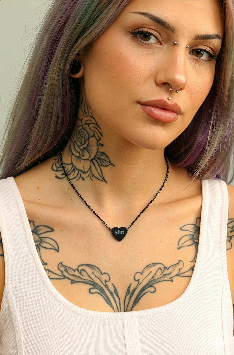 Woman with tattoos wearing a black heart-shaped pendant necklace.