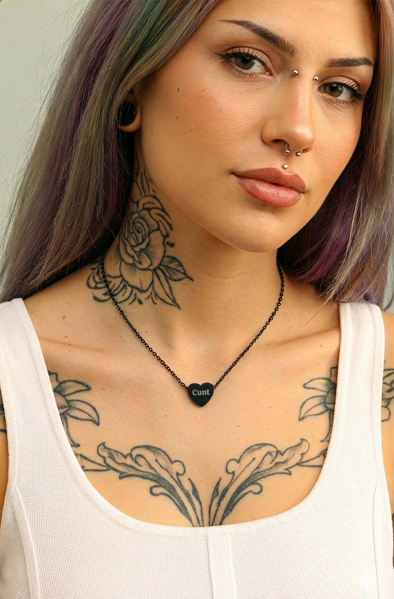 Woman with tattoos wearing a black heart-shaped pendant necklace.