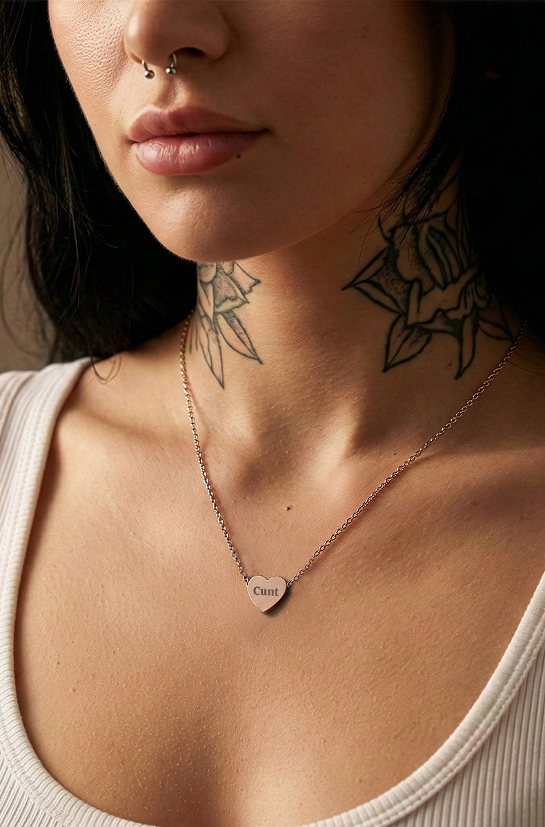 Close-up of a person wearing a necklace with a heart pendant, showing tattoos on the neck.