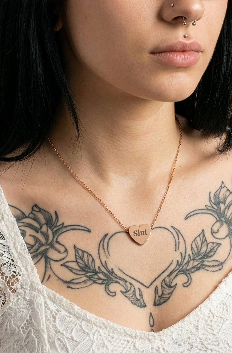 Person wearing a necklace with a heart-shaped pendant, surrounded by tattoos on the neck and shoulders.