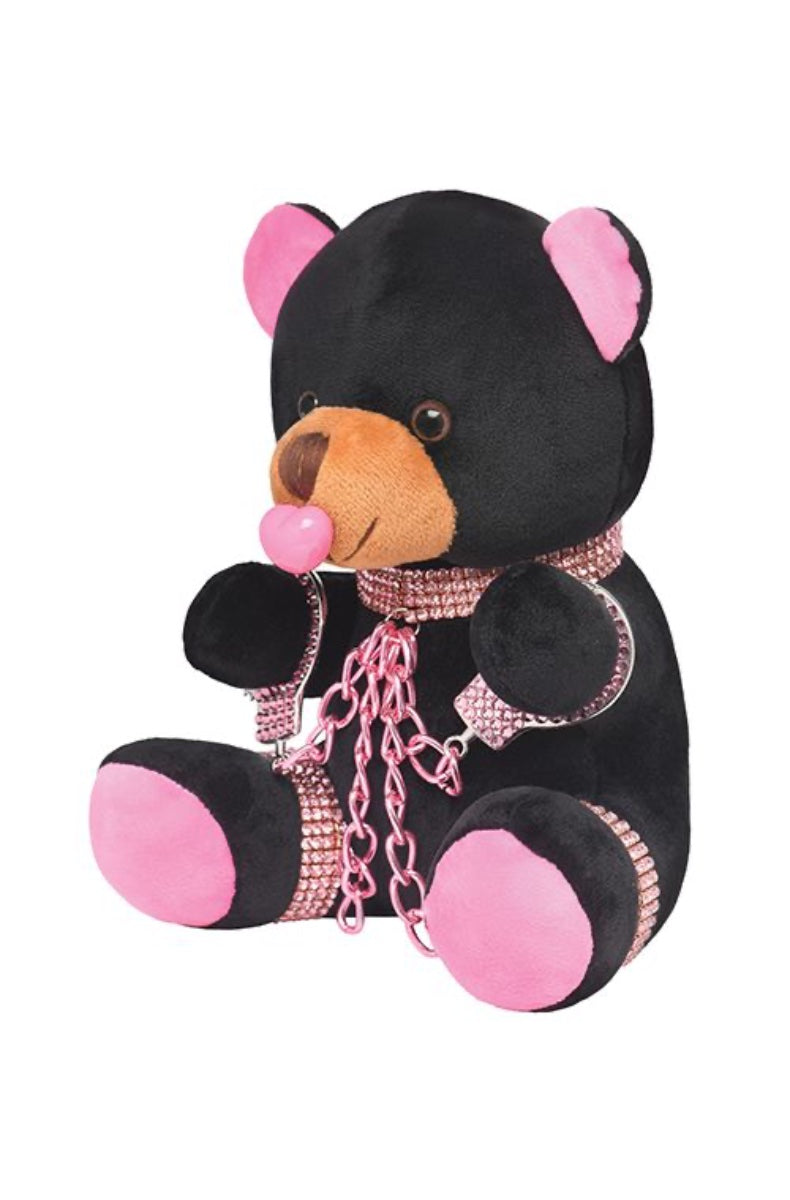 side view of black plush teddy bear with pink rhinestone bondage accessories against white background