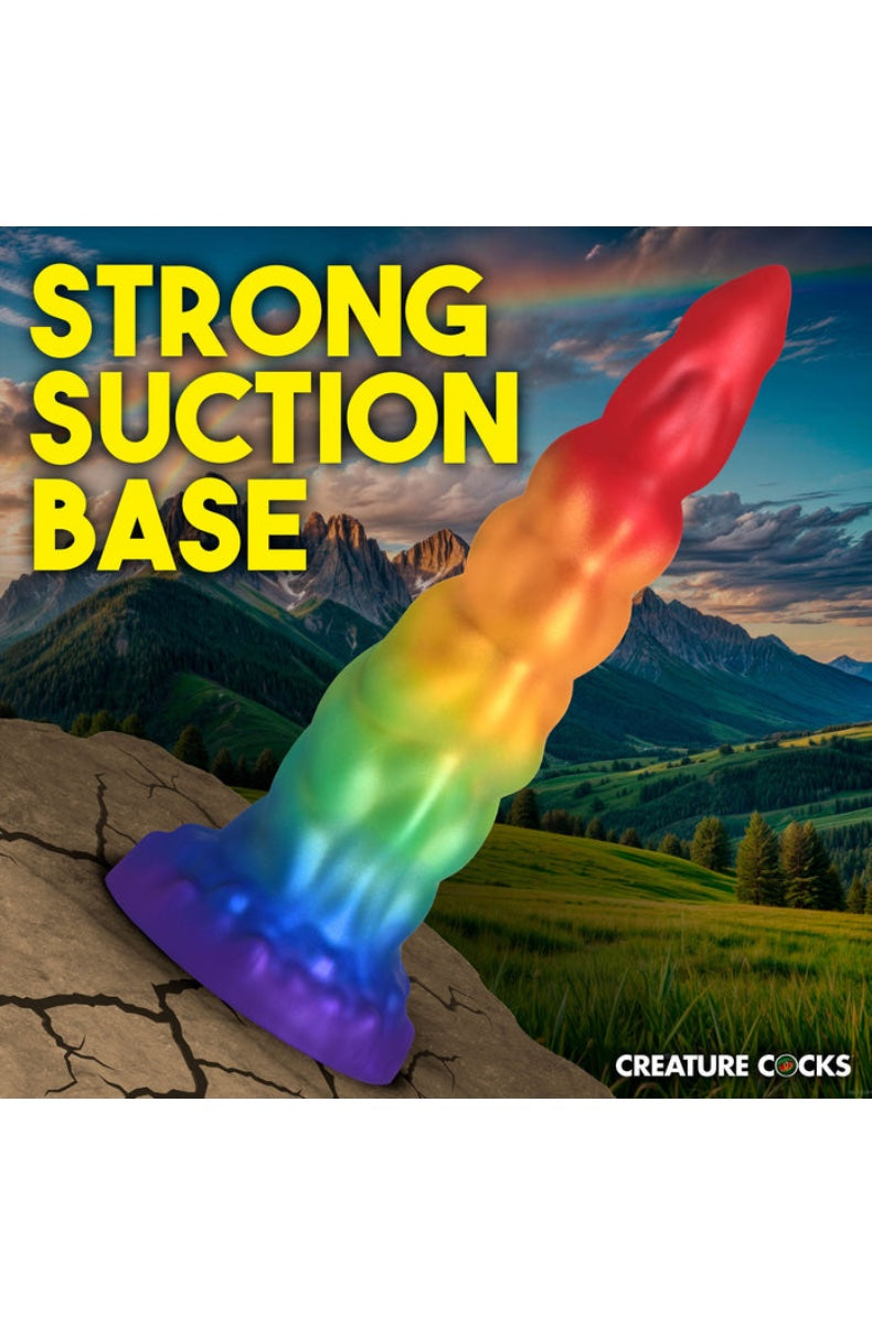Rainbow dildo positioned on rocky surface with "Strong Suction Base" text overlay against mountain backdrop