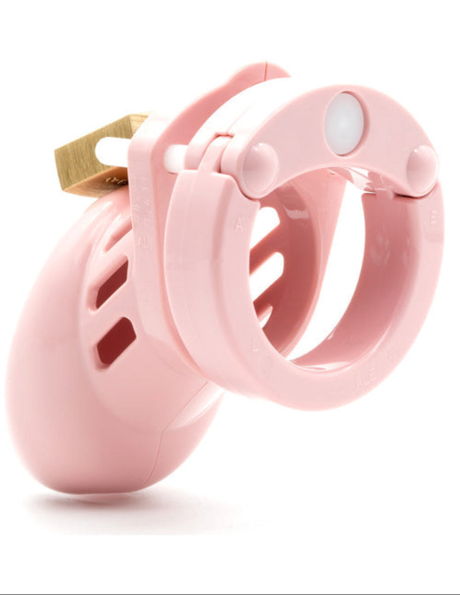Pink chastity cage with brass padlock locked at the top, showing the U-ring with size markings, on white.