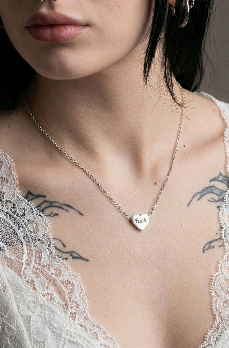 Model wearing silver heart pendant necklace with white lace top and neck tattoos