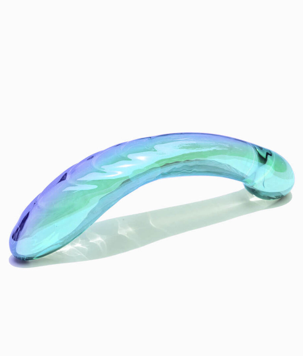 Iridescent blue-green glass G-spot dildo lying on its side, showing the curved ribbed shaft and rounded bulb end, on white.