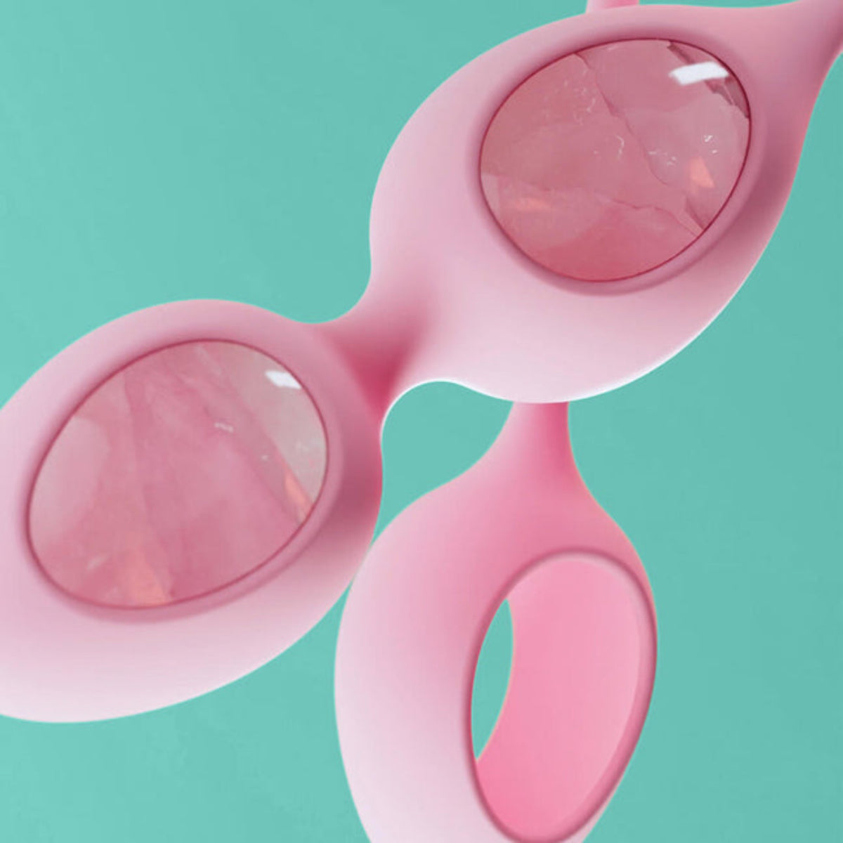 Macro close-up of rose quartz crystal seen through the pink silicone holder windows, with a pull loop, on a mint background.