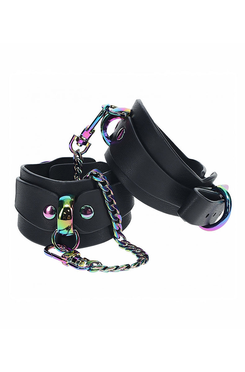 Pair of wide black bonded leather wrist cuffs with iridescent rainbow metal D-rings and a connecting chain with a snap clip.