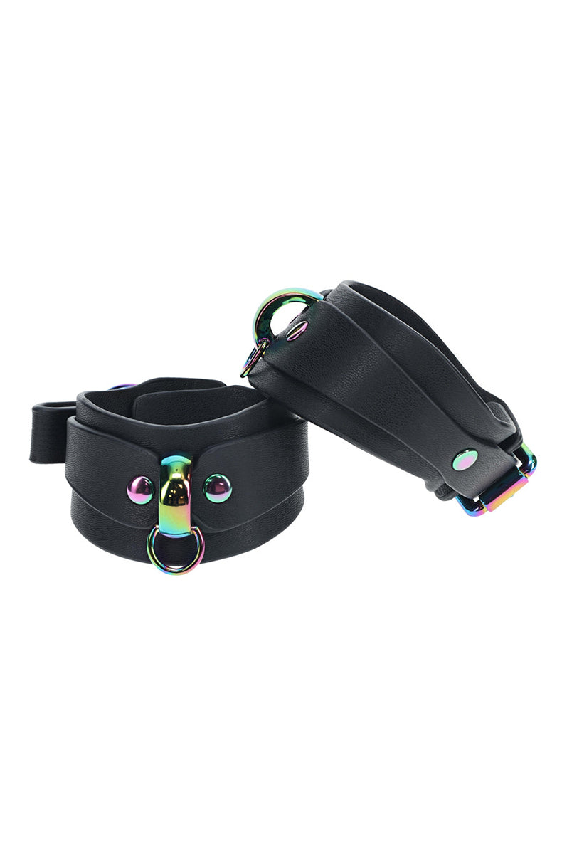 Detail view of one black bonded leather wrist cuff with rainbow buckle, D-ring, and rainbow snap rivets.