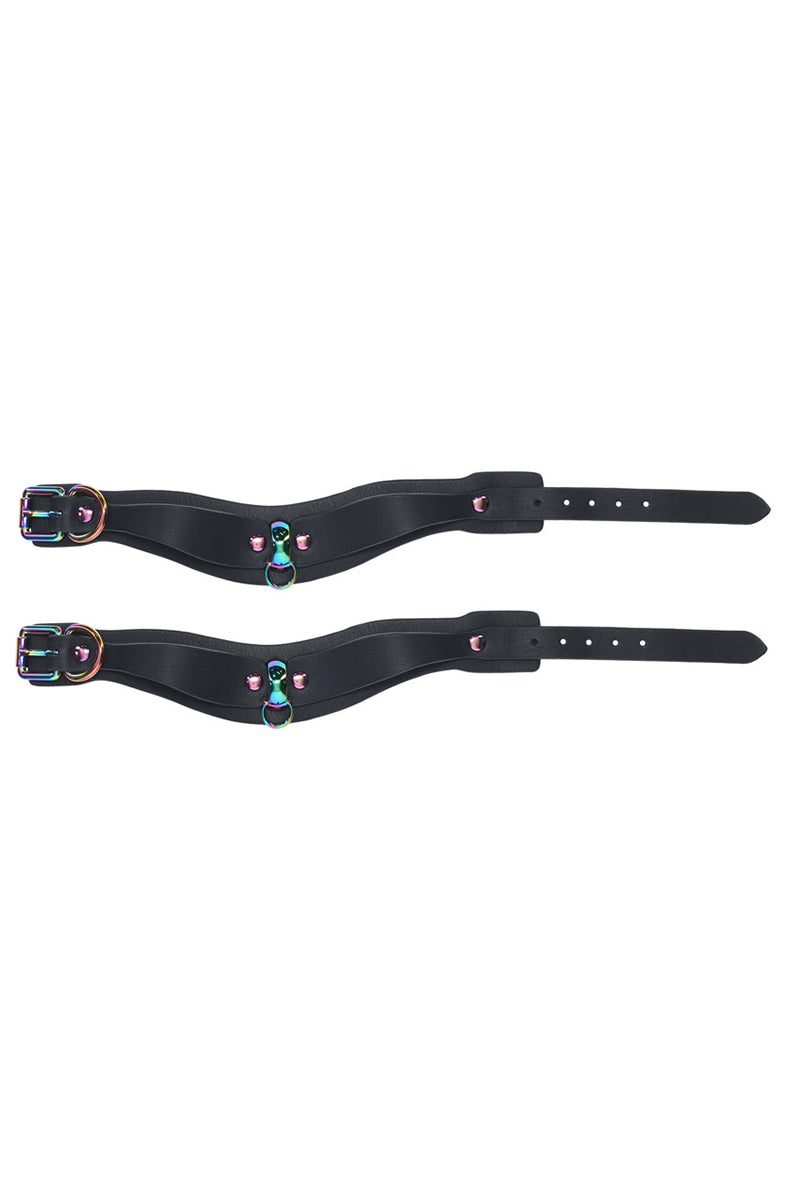 Stacked pair of black bonded leather wrist cuffs showing rainbow D-rings, rivets, and inner edge.