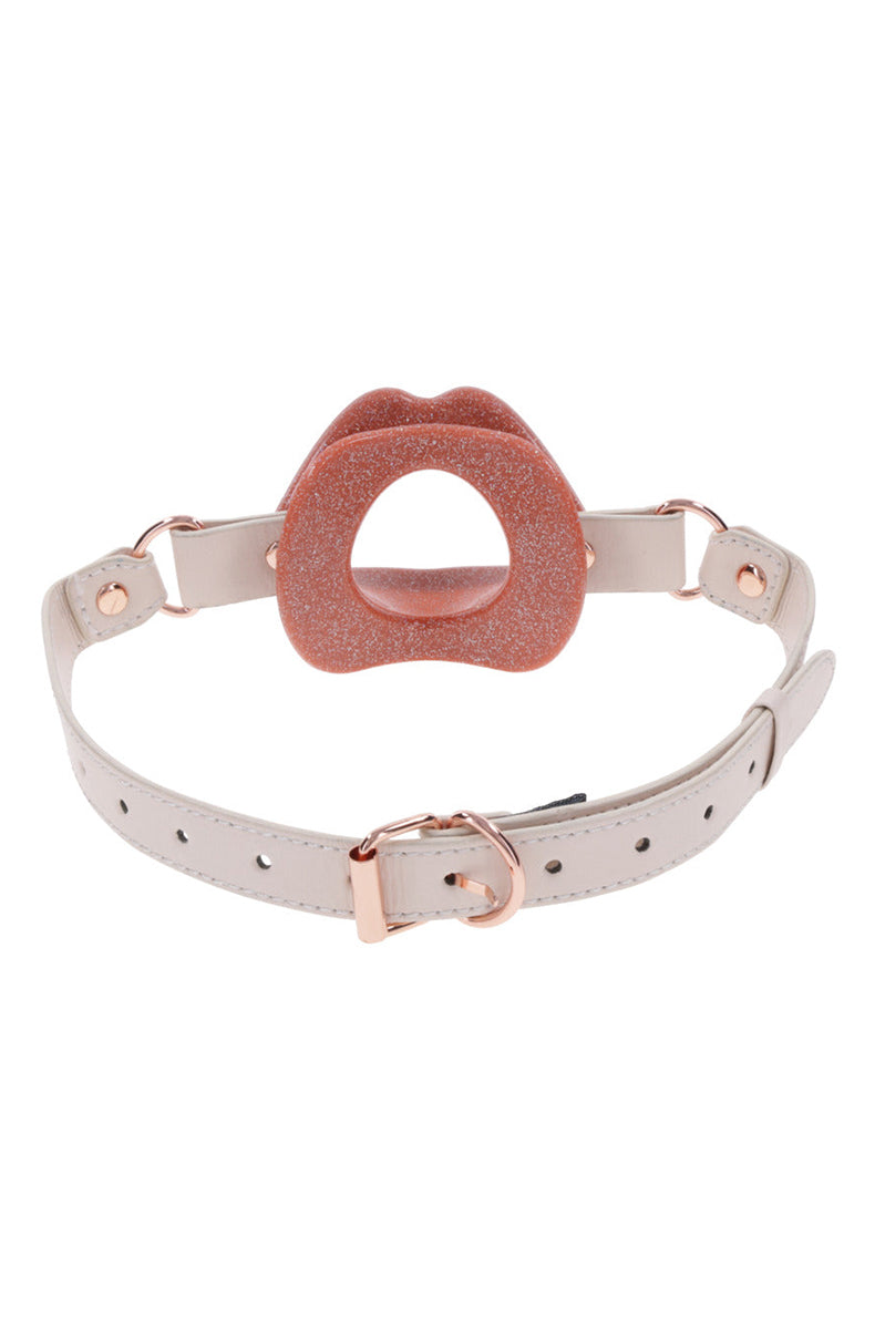 Side view of peach lips gag with cream faux leather strap and rose-gold buckle laid flat.