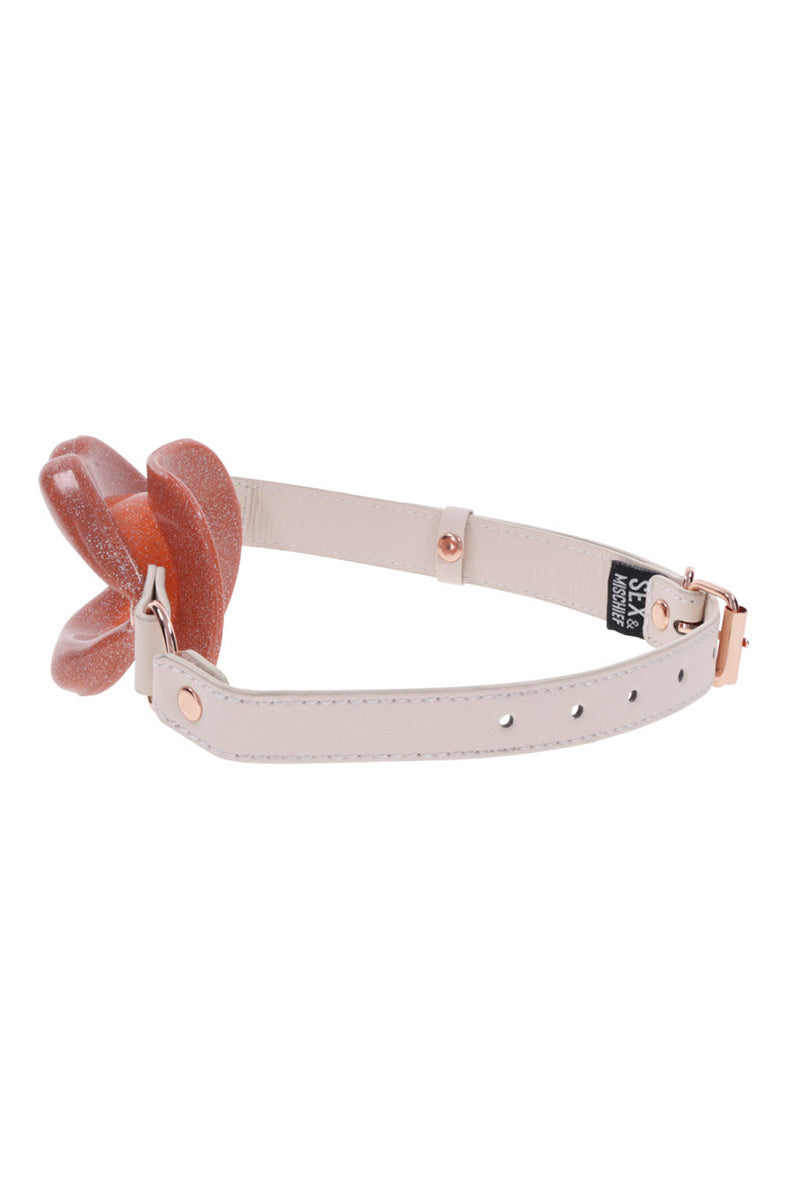 Detail view of rose-gold buckle and adjustment holes on the cream faux leather strap of the lips gag.