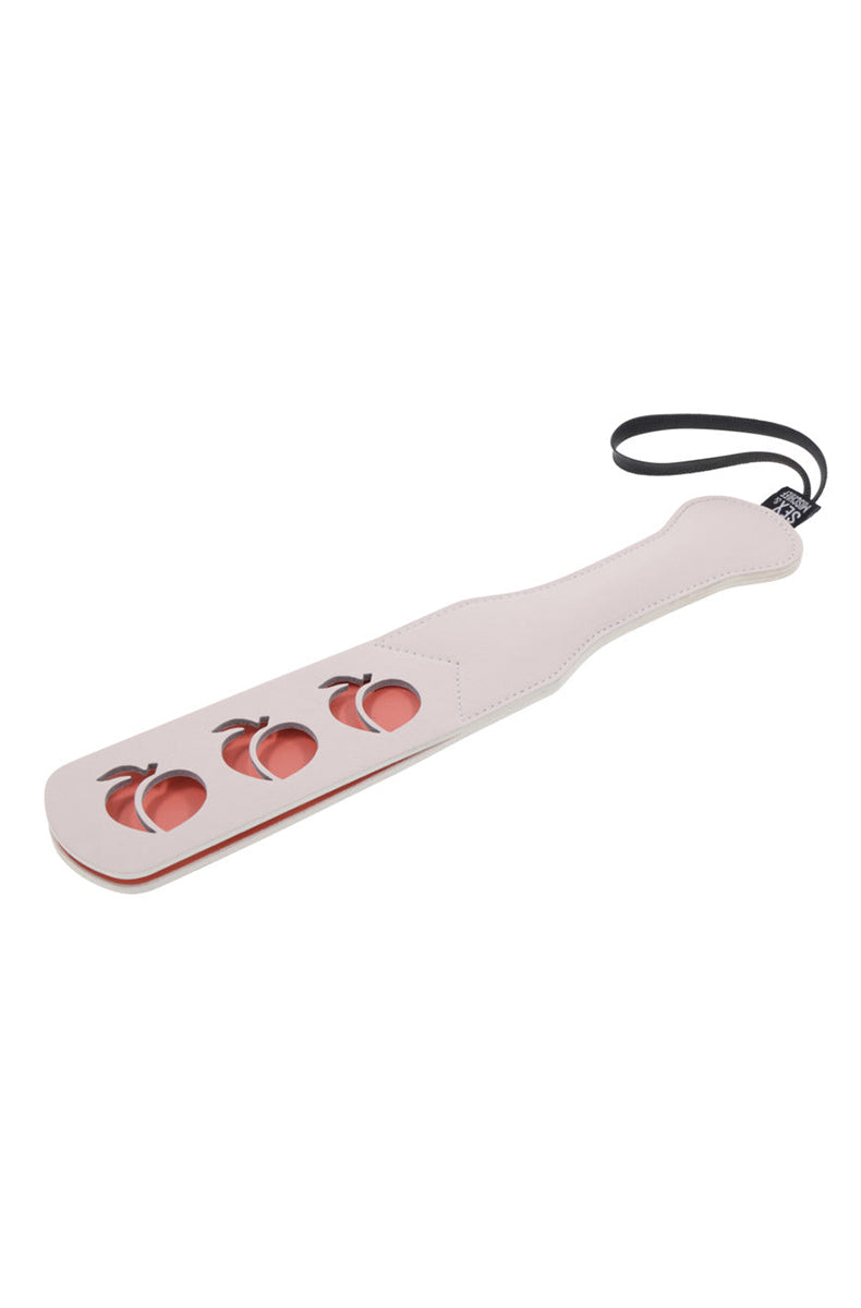 Front view of cream paddle showing three peach cutouts revealing a coral inner layer with a black wrist loop and brand tag.