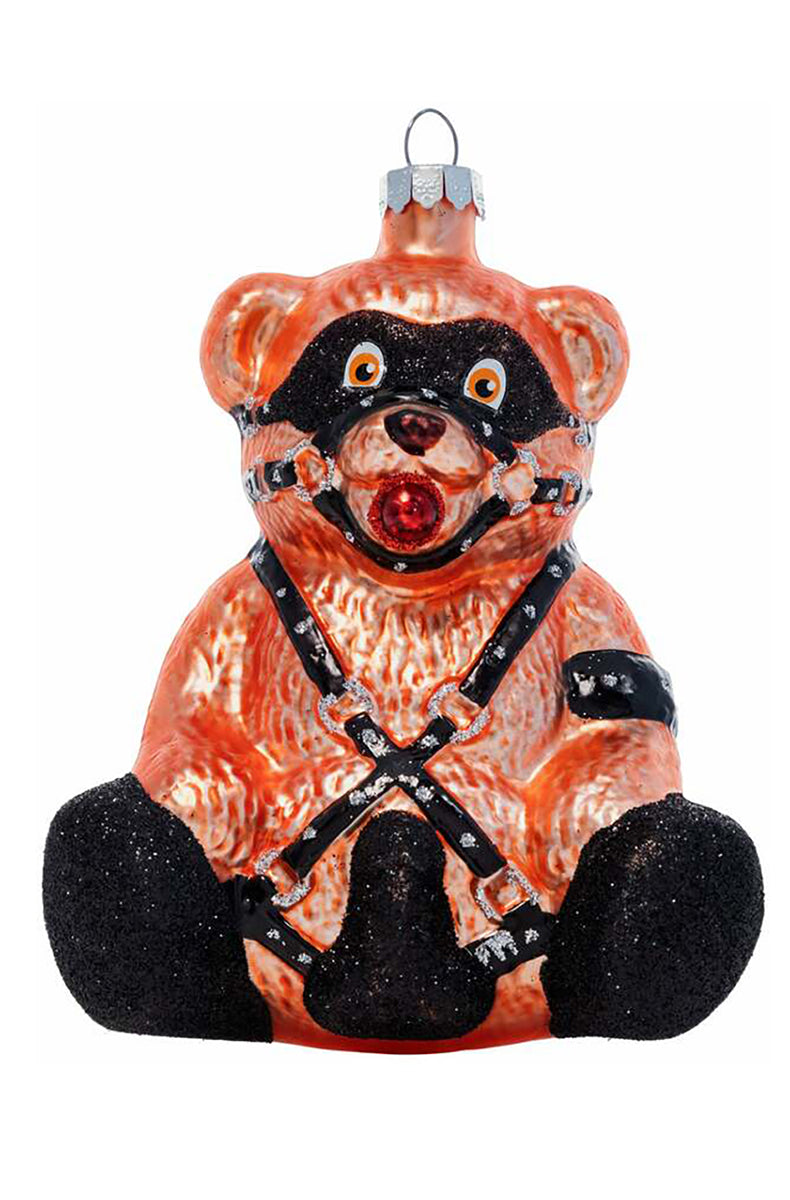 Hand-blown glass ornament of an orange-brown seated teddy bear in black eye mask, harness, ball gag, and glitter feet.