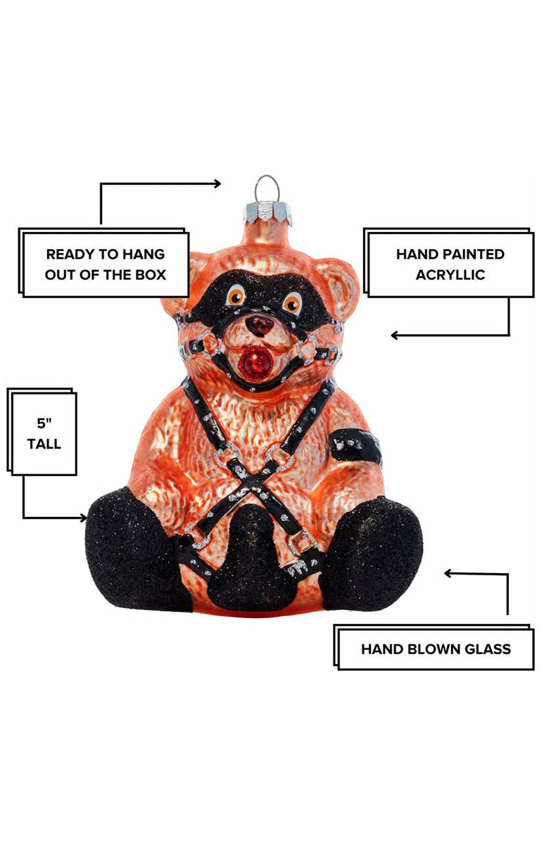 Close-up of black eye mask and ball gag on hand-blown glass orange-brown teddy bear ornament.