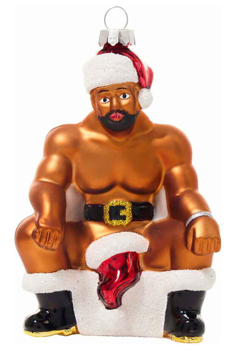 Hand-blown glass ornament of a muscular bearded man in Santa hat and black boots seated on a snowy chimney with red sock.