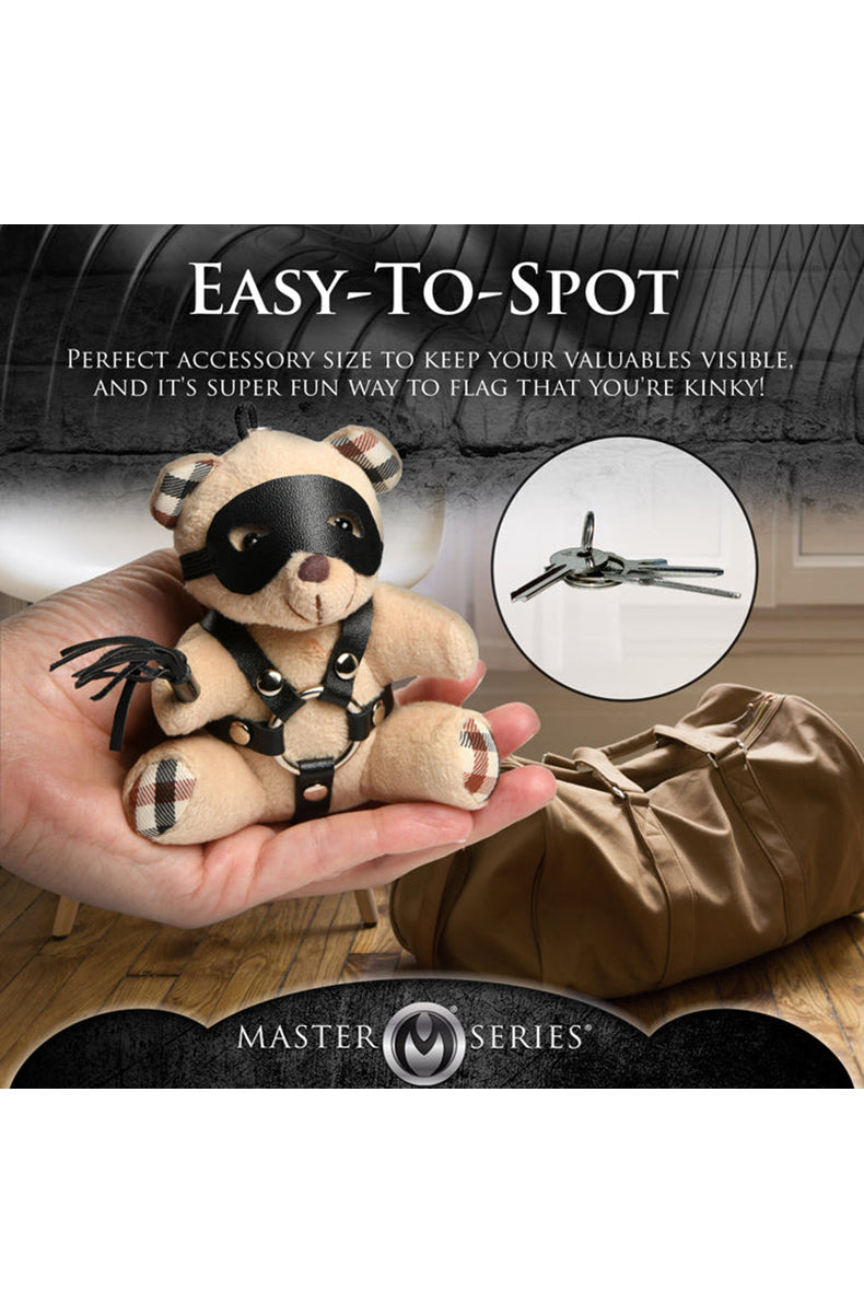 Detail view of mini black flogger held by tan plush teddy bear keychain paw.