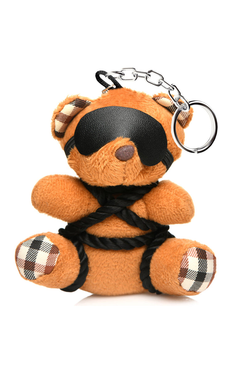 Tan plush teddy bear keychain tied with black silky shibari rope across the chest and arms, with a black blindfold.