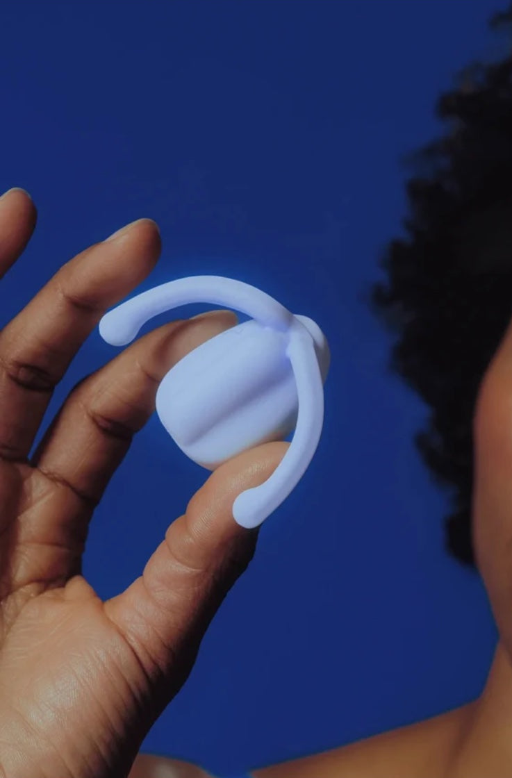 Hand holding lavender wearable vibrator against blue background showing compact size