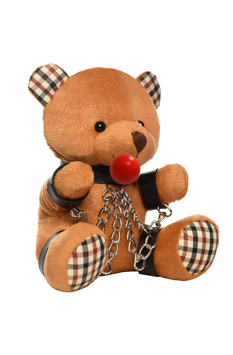 Side view of tan plush teddy bear in black collar and cuffs with silver chains and red ball gag strap visible.