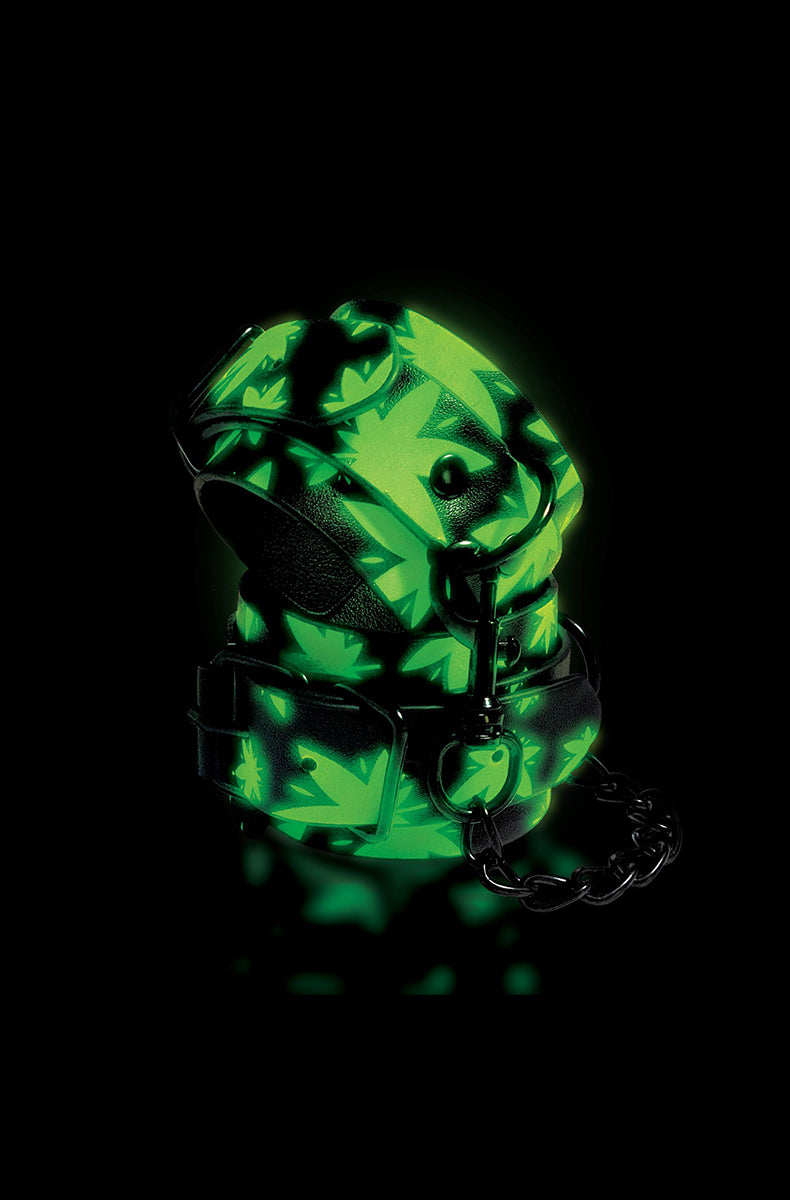 Glow-in-the-dark view of the cannabis-leaf ankle cuffs glowing green against a black background.