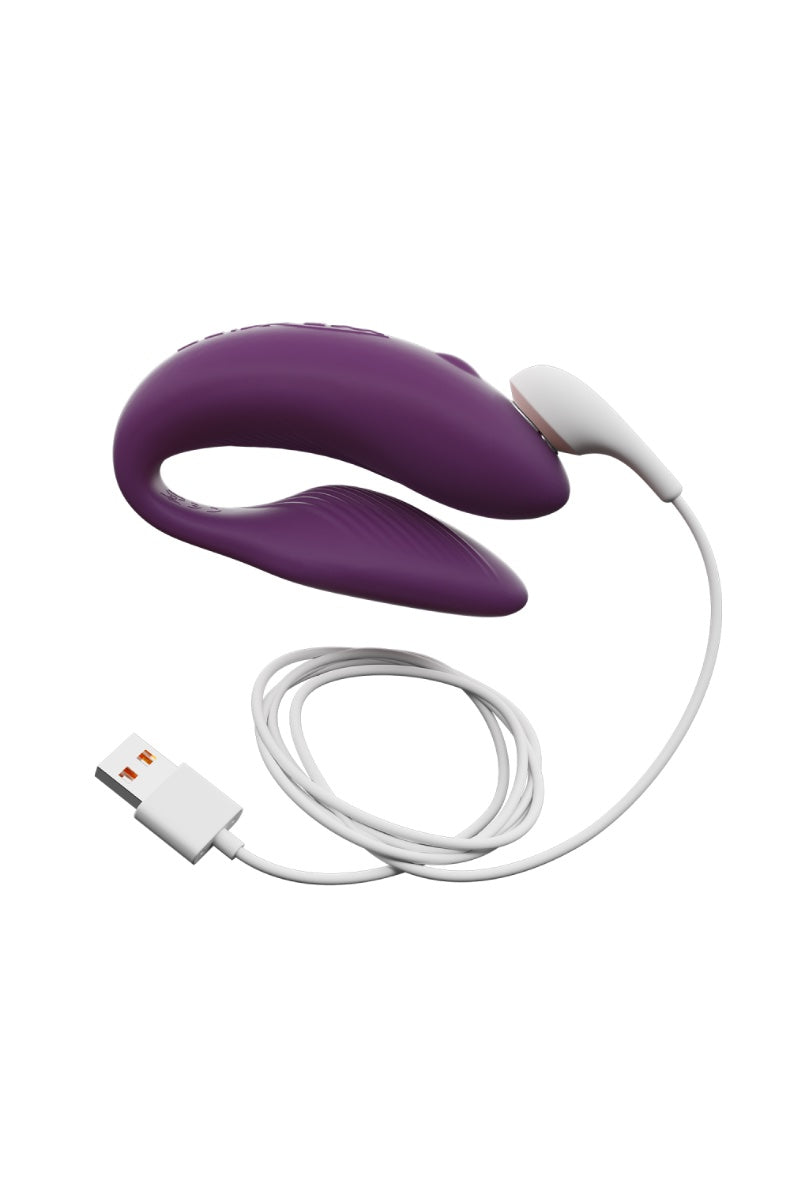 Purple C-shaped couples vibrator with charging cable and white USB adapter on white background
