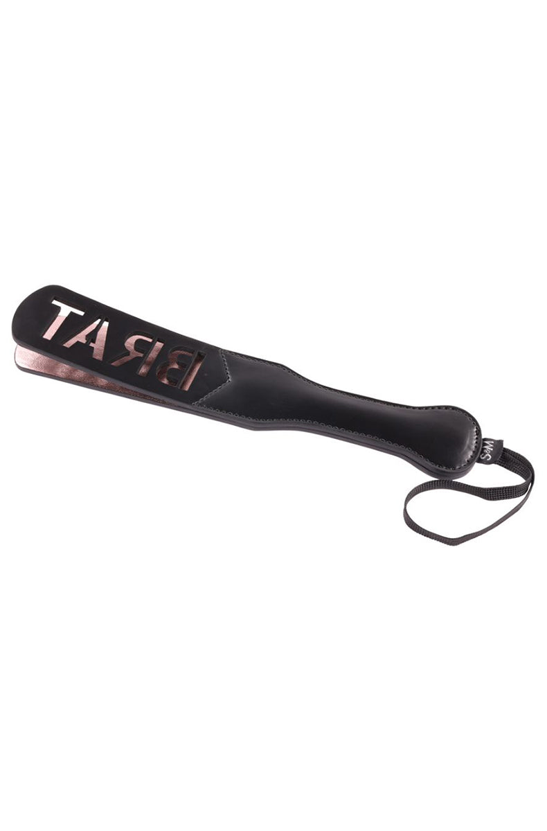 Black faux leather paddle with BRAT cutout lettering over a rose-gold backing, layered build, and a black wrist loop.