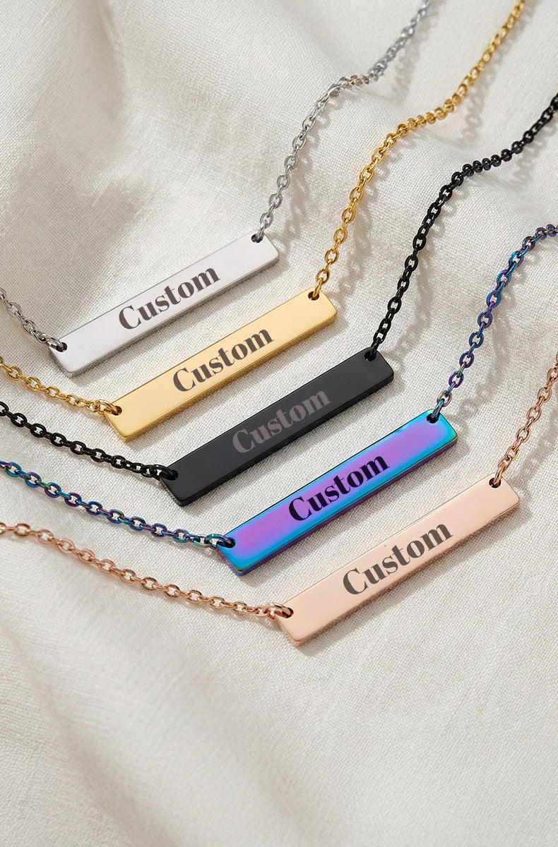Five custom engraved bar necklaces showing silver, gold, black, rainbow holographic, and rose gold finishes with "Custom" text