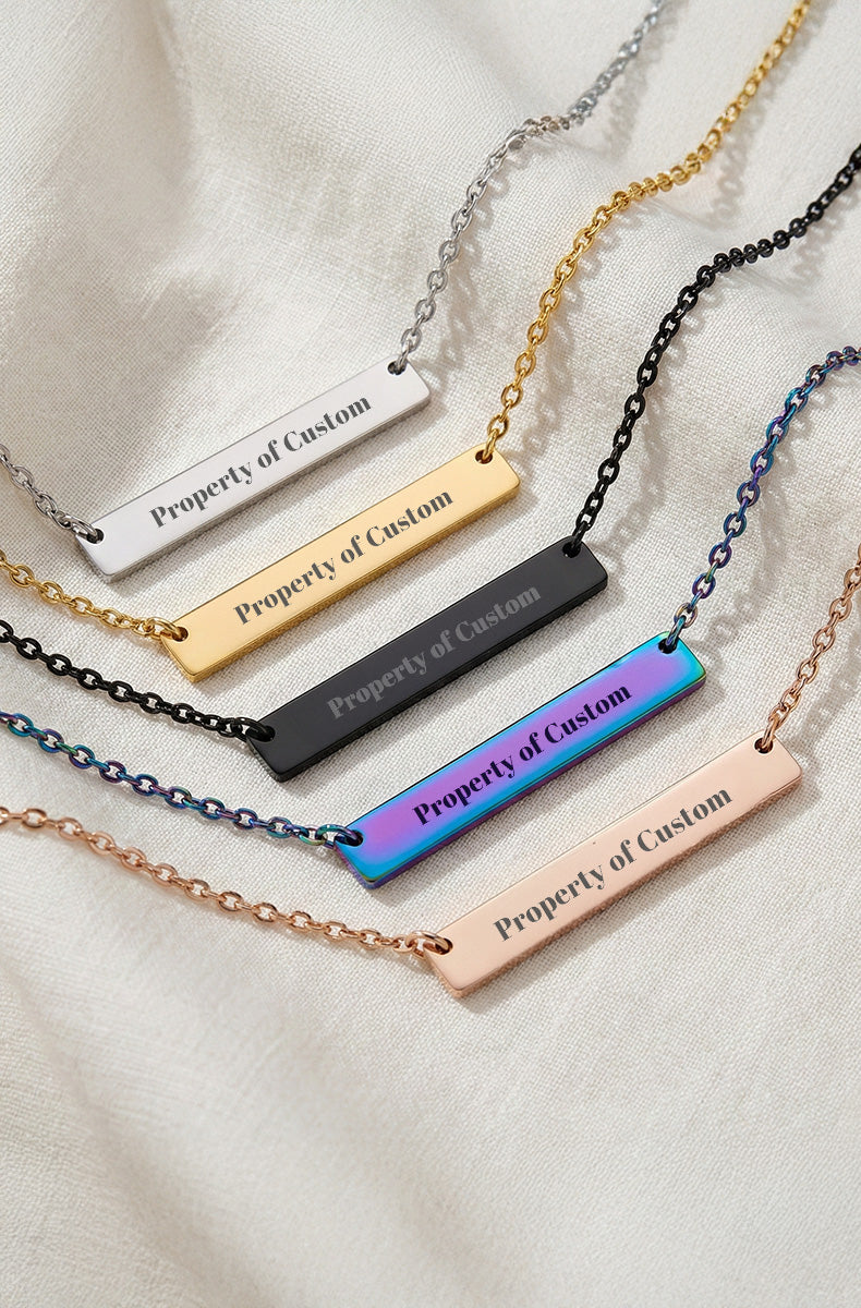 Necklaces with 'Property of Custom' bar pendants in various colors on a light fabric background