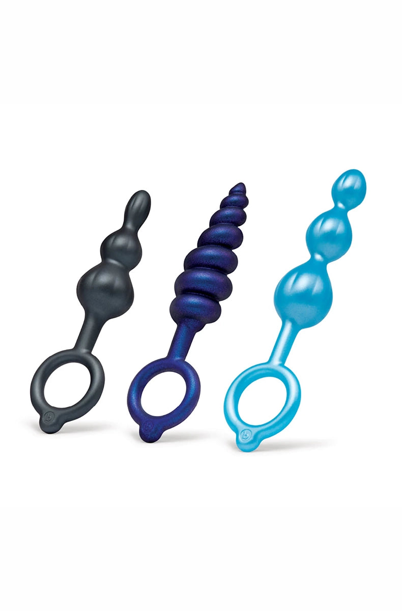 Three anal plugs standing side by side: black and teal smooth beads, midnight blue swirl, each with a finger ring.