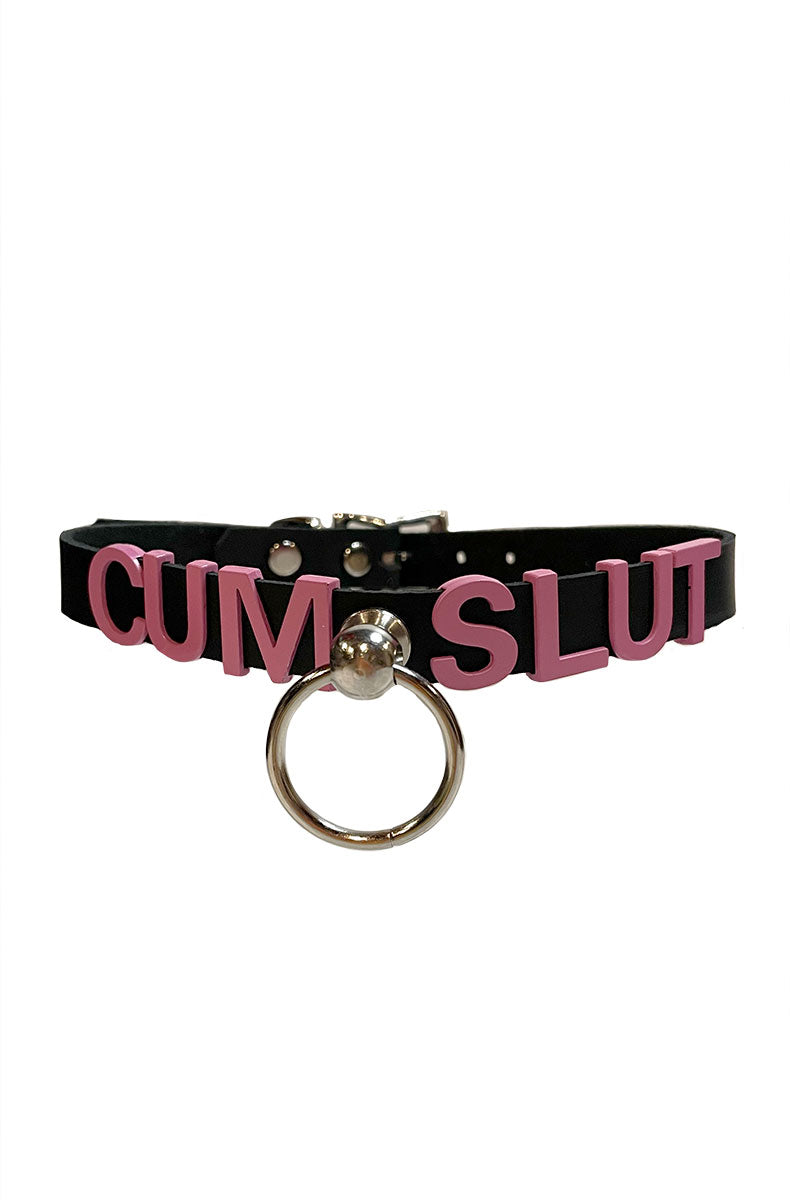 Black vegan-leather collar with "CUM SLUT" in bold pink lettering and a silver metal O-ring at the front center.