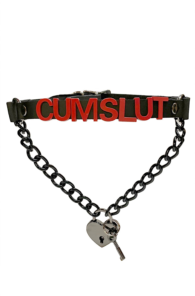 Black vegan-leather collar with "CUMSLUT" in bold red lettering, a black chain swag draping below, and a silver heart-shaped padlock with a silver key.