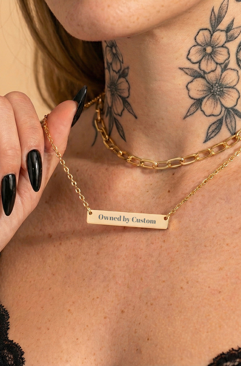 Close-up of gold bar necklace worn on tattooed model's neck with gold chain