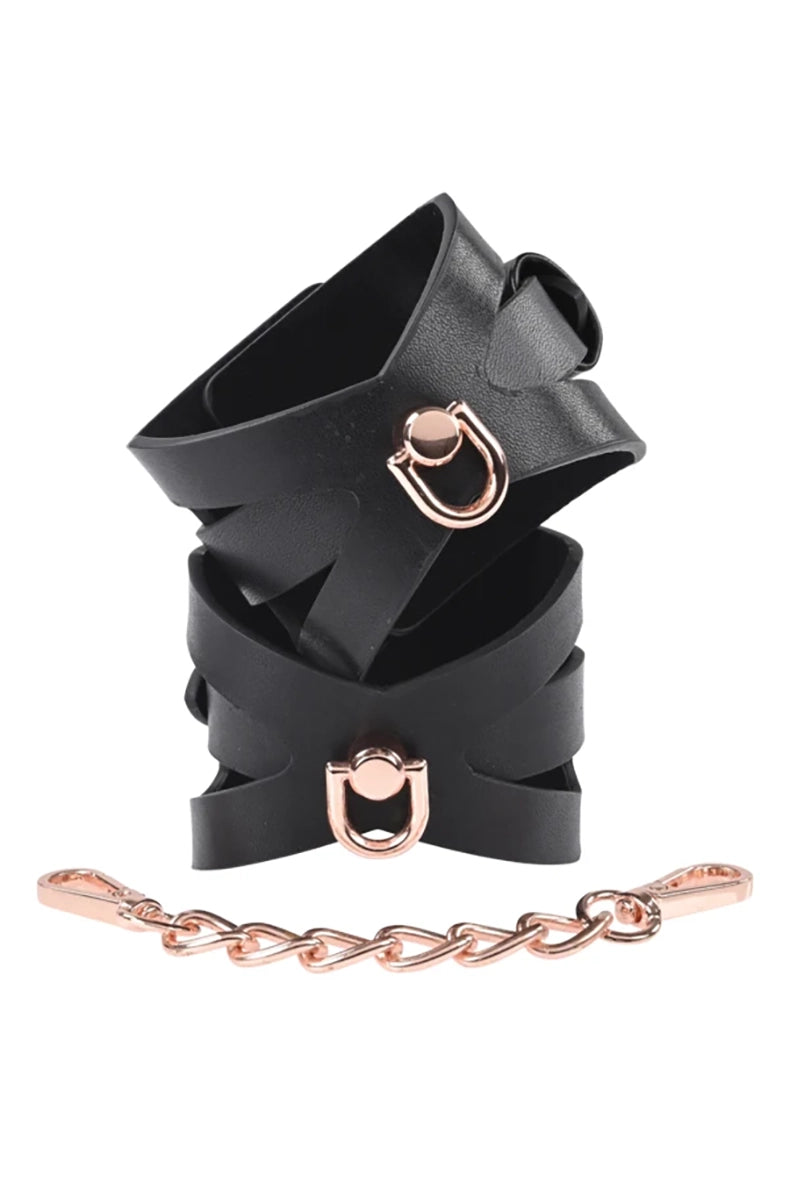 Pair of black faux leather wrist cuffs with corset cutout bands, rose-gold D-rings, and a short rose-gold connecting chain.